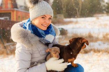 Genç bir kadın dışarıda karda eğleniyor. Dişi, soğuk kış gününde küçük safkan köpekleriyle oynuyor..