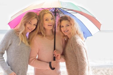 Renkli şemsiye altında üç güzel bayan arkadaş. Süveter giyen şık kadınlar dışarıda vakit geçiriyorlar..