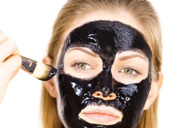 Siyah detoks detoks ile uygulanan genç bir kadın maskesini yüzüne doğru sıyırdı. Deriyle ilgilenen bir kız. Güzellik tedavisi. Cilt bakımı.