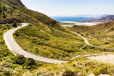 İspanyol dağları manzarası ve vadide birçok serası olan deniz kıyısı manzarası. Castillitos Bataryası 'na giden dolambaçlı yol.