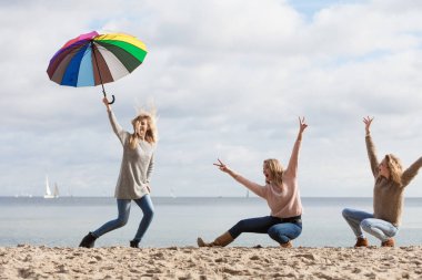 Üç kadın renkli şemsiyelerle hoplayıp zıplıyor. Bayan arkadaşlar dışarıda eğleniyor..