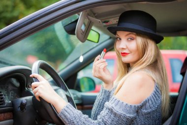 Dikiz aynasına bakan, dudaklarını boyayan, arabayı sürerken makyaj yapan çekici genç bir kadın..