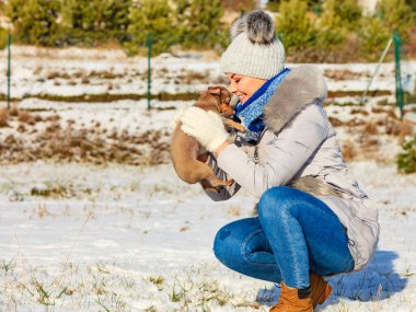 Genç bir kadın dışarıda karda eğleniyor. Dişi, soğuk kış gününde safkan köpek yavrusuyla oynuyor..