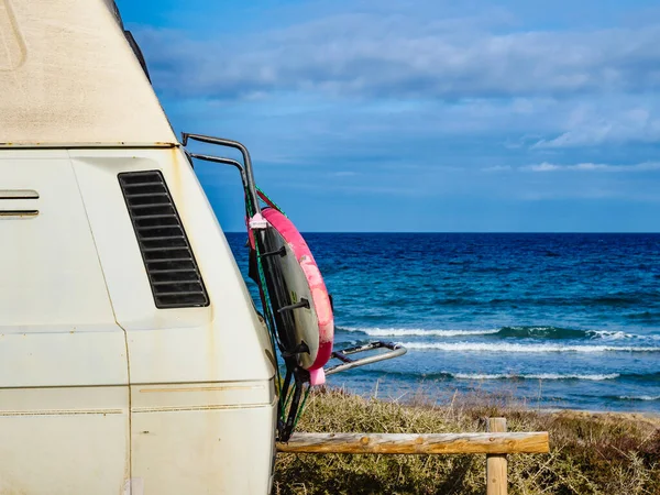 Camper van with surf board camping on beach sea shore. Holidays, sport and adventure concept.