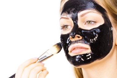 Siyah detoks detoks ile uygulanan genç bir kadın maskesini yüzüne doğru sıyırdı. Deriyle ilgilenen bir kız. Güzellik tedavisi. Cilt bakımı.