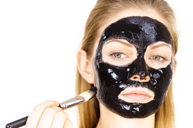 Siyah detoks detoks ile uygulanan genç bir kadın maskesini yüzüne doğru sıyırdı. Deriyle ilgilenen bir kız. Güzellik tedavisi. Cilt bakımı.