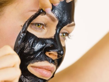 Karbonhidratlı siyah maskesini yüzünden, beyazın üstüne çıkaran genç bir kadın. Genç kız yağlı cildiyle ilgileniyor, gözenekleri temizliyor. Güzellik tedavisi. Cilt bakımı.