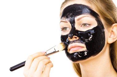 Siyah detoks detoks ile uygulanan genç bir kadın maskesini yüzüne doğru sıyırdı. Deriyle ilgilenen bir kız. Güzellik tedavisi. Cilt bakımı.