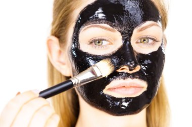 Siyah detoks detoks ile uygulanan genç bir kadın maskesini yüzüne doğru sıyırdı. Deriyle ilgilenen bir kız. Güzellik tedavisi. Cilt bakımı.