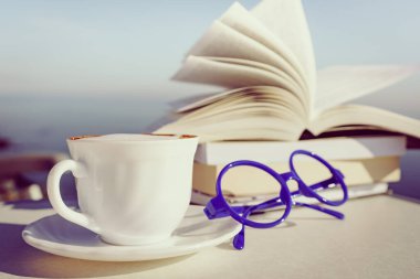 Tatillerde kitap okumak. Kahve fincanı ve kitaplar açık havada mavi deniz suyuna karşı. Kitap sayfaları rüzgarda çırpınıyor.