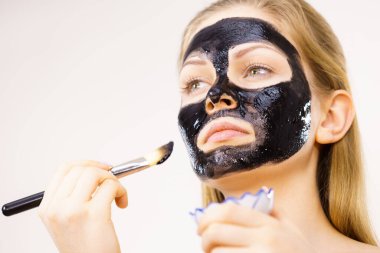 Yüzüne siyah detoks çamur maskesi süren genç bir kadın. Deriyle ilgilenen bir kız. Güzellik tedavisi. Cilt bakımı.