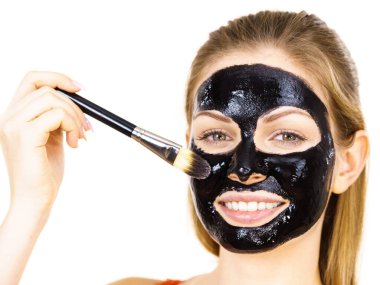 Siyah detoks detoks ile uygulanan genç bir kadın maskesini yüzüne doğru sıyırdı. Deriyle ilgilenen bir kız. Güzellik tedavisi. Cilt bakımı.