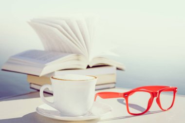 Tatillerde kitap okumak. Kahve fincanı ve kitaplar açık havada mavi deniz suyuna karşı. Kitap sayfaları rüzgarda çırpınıyor.