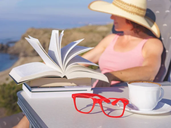 休日の読書 成熟した観光客の女性は海岸でリラックスし 本を読み 崖から海の景色をお楽しみください コーヒーカップとグラスに焦点を当てる — ストック写真
