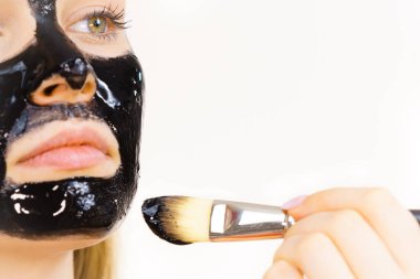 Siyah detoks detoks ile uygulanan genç bir kadın maskesini yüzüne doğru sıyırdı. Deriyle ilgilenen bir kız. Güzellik tedavisi. Cilt bakımı.