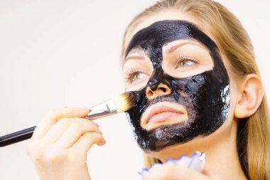 Yüzüne siyah detoks çamur maskesi süren genç bir kadın. Deriyle ilgilenen bir kız. Güzellik tedavisi. Cilt bakımı.