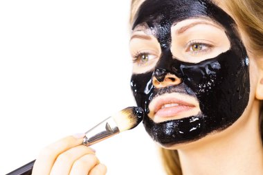 Siyah detoks detoks ile uygulanan genç bir kadın maskesini yüzüne doğru sıyırdı. Deriyle ilgilenen bir kız. Güzellik tedavisi. Cilt bakımı.