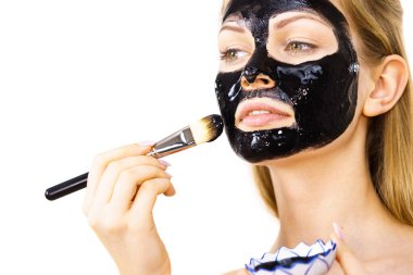 Siyah detoks detoks ile uygulanan genç bir kadın maskesini yüzüne doğru sıyırdı. Deriyle ilgilenen bir kız. Güzellik tedavisi. Cilt bakımı.