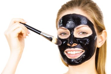 Siyah detoks detoks ile uygulanan genç bir kadın maskesini yüzüne doğru sıyırdı. Deriyle ilgilenen bir kız. Güzellik tedavisi. Cilt bakımı.