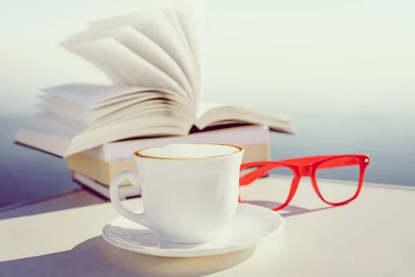休日の読書 青い海の水の背景に対して屋外テーブルの上のコーヒーカップと本 風になびく本のページ — ストック写真