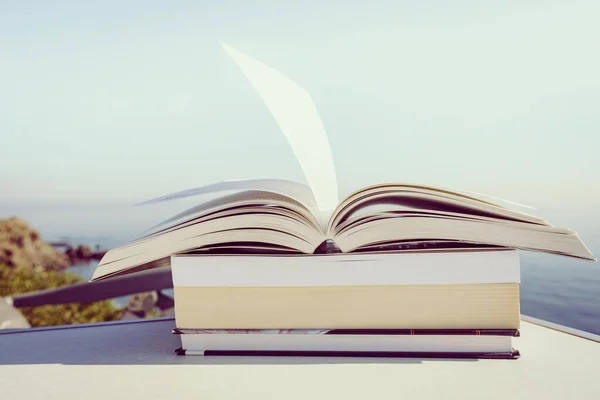 休日の読書 青い海の背景を背景に屋外のテーブルの上のオープンブック 風になびく本のページ — ストック写真