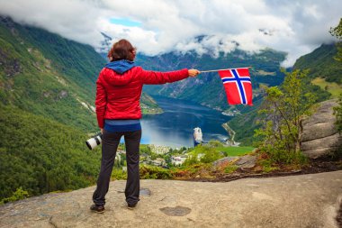 Flydalsjuvet bakış açısından fiyort Geirangerfjorden üzerinde manzaranın tadını çıkaran kadın turist Norveç bayrağını tutuyor. Seyahat ve seyahat.