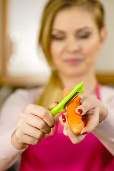 Woman peeling vegetables using food peeler. Cooking female preparing carrot before serving.
