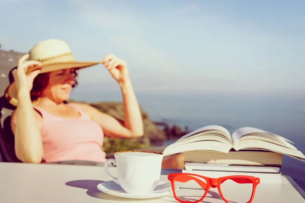 休日の読書 成熟した観光客の女性は海岸でリラックスし 本を読み 崖から海の景色をお楽しみください コーヒーカップとグラスに焦点を当てる — ストック写真