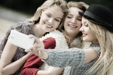 Üç kadın selfie çekiyor, dışarıda eğleniyor, fotoğraf çekmek için akıllı telefon kullanıyor..