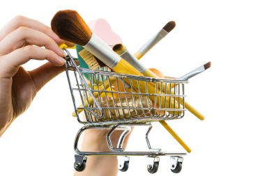 Elinde makyaj fırçası gibi güzellik aksesuarlarıyla dolu alışveriş arabası tutan bir kadın..