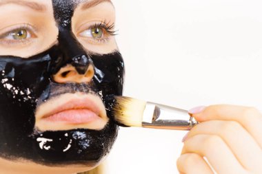 Siyah detoks detoks ile uygulanan genç bir kadın maskesini yüzüne doğru sıyırdı. Deriyle ilgilenen bir kız. Güzellik tedavisi. Cilt bakımı.