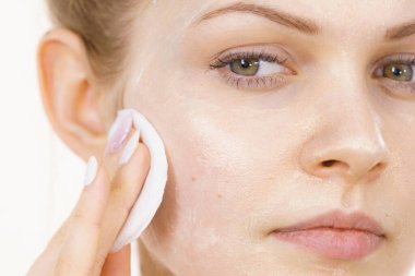 Yüzünde maske olan genç bir kadın pamuklu bezle kozmetiği temizliyor. Cildiyle ilgilenen genç bir kız. Güzellik tedavisi. Cilt bakımı.