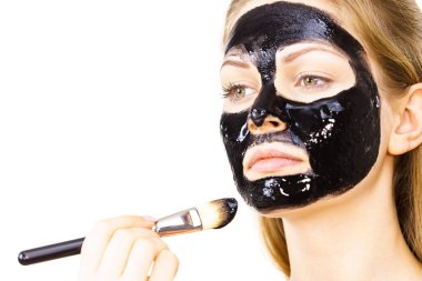 Siyah detoks detoks ile uygulanan genç bir kadın maskesini yüzüne doğru sıyırdı. Deriyle ilgilenen bir kız. Güzellik tedavisi. Cilt bakımı.