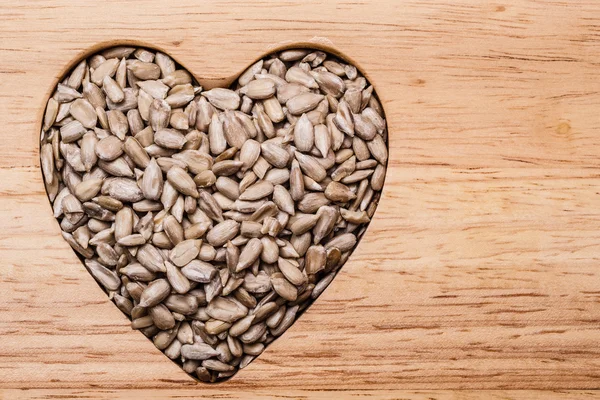 Nasiona słonecznika na powierzchni drewna w kształcie serca — Zdjęcie stockowe