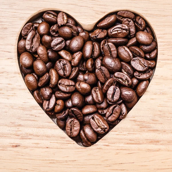 Kávová zrna na dřevěné desce ve tvaru srdce — Stock fotografie