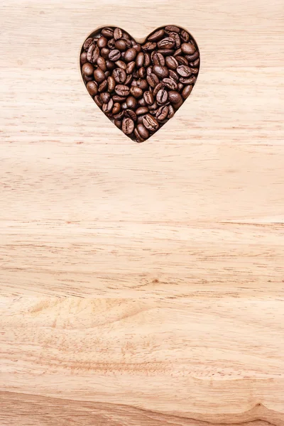 Grains de café en forme de coeur sur planche en bois — Photo