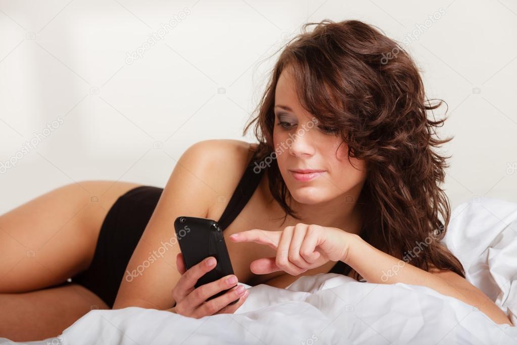 Sexy lazy girl lying with phone on bed in bedroom