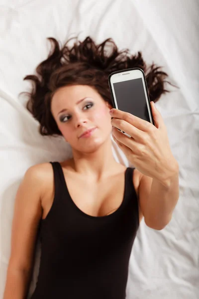 Sexy lazy girl lying with phone on bed in bedroom — Stock Photo, Image