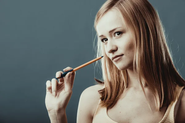Blonde girl thinking holds pen on gray background — Stockfoto
