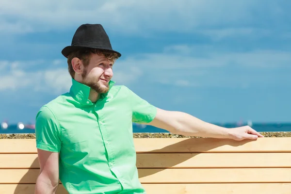 Young hipster man sitting on bench near the sea outdoor — Stock Photo, Image