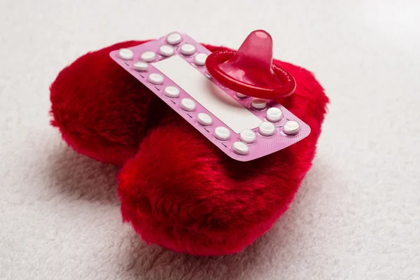 Противозачаточные таблетки и презерватив на красном сердце — стоковое фото