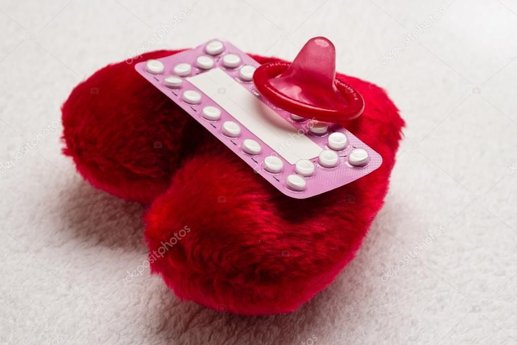 Contraceptive pills and condom on red heart