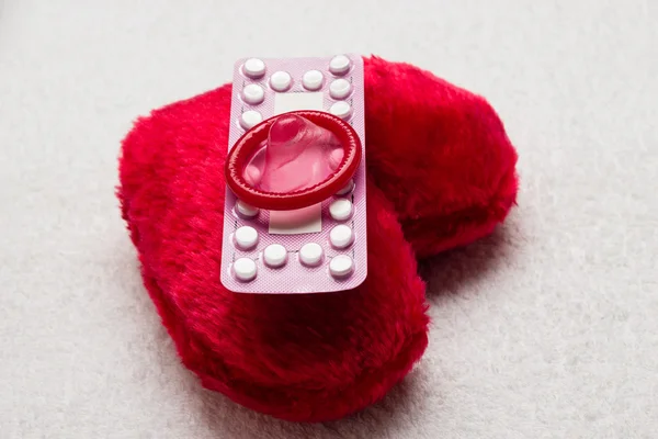 Tabletki antykoncepcyjne i prezerwatywy na czerwone serce — Zdjęcie stockowe