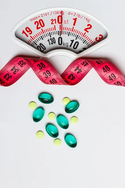 Pills with measuring tape on white scales — Stock Photo, Image