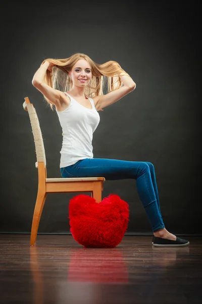 Happy woman with heart shaped pillow on floor — ストック写真