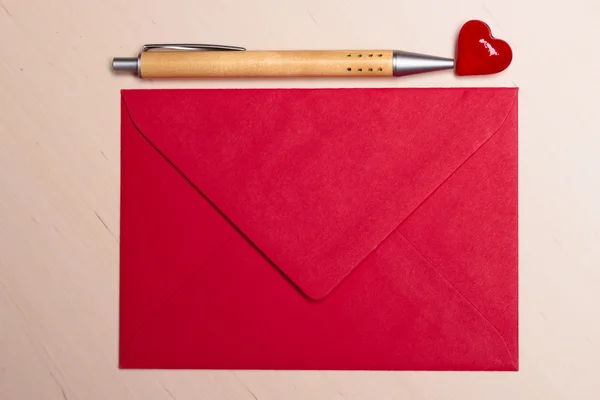 Busta rossa cuore e penna sul tavolo — Foto Stock