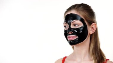 Yüzünde karbonhidrat maskesi olan genç bir kadın kameraya ve yana, beyaza bakıyor. Güzellik tedavisi. Cilt bakımı.