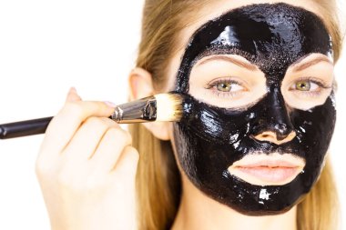 Siyah detoks detoks ile uygulanan genç bir kadın maskesini yüzüne doğru sıyırdı. Deriyle ilgilenen bir kız. Güzellik tedavisi. Cilt bakımı.