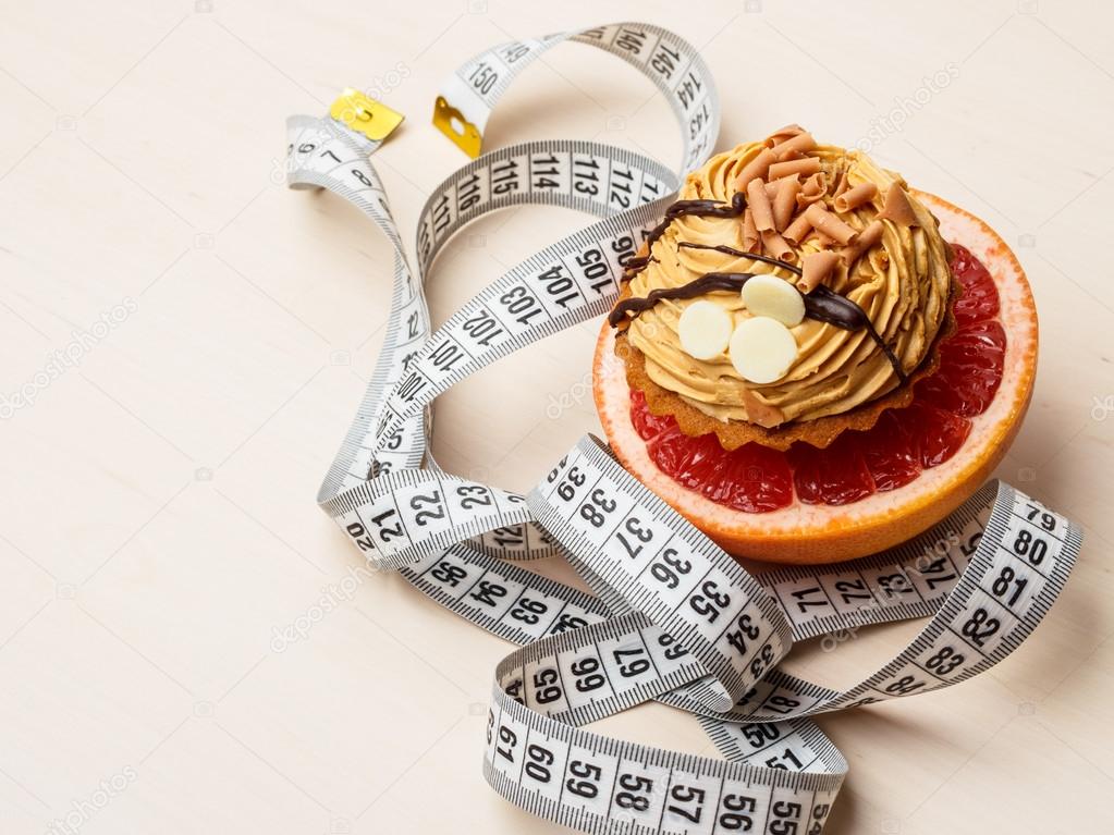 Grapefruit and cake with measuring tape. Diet
