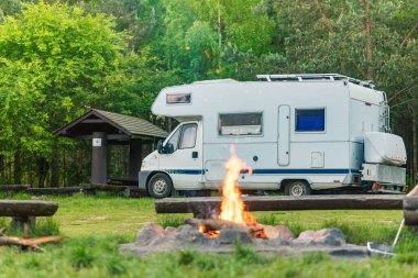 Gece kamp ateşi yüksek ağaçların arasına park edilmiş bir karavanın önünde çatırdıyor. Ateşin sıcaklığı, serin orman havasıyla çelişiyor. Rahatlamak için huzurlu bir atmosfer yaratıyor..